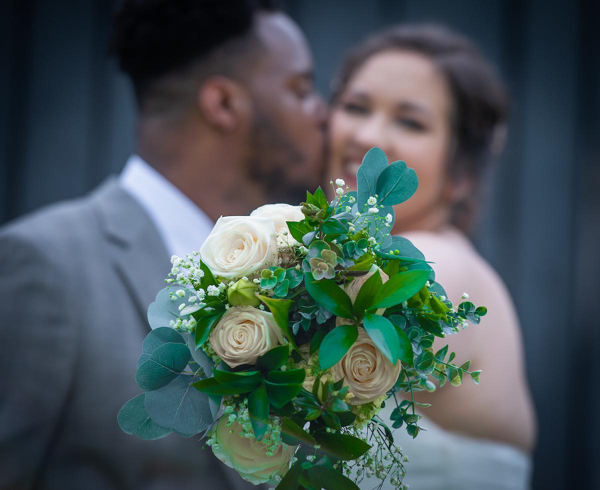 upclose of a wedding bouquet and a bride and groom in the background