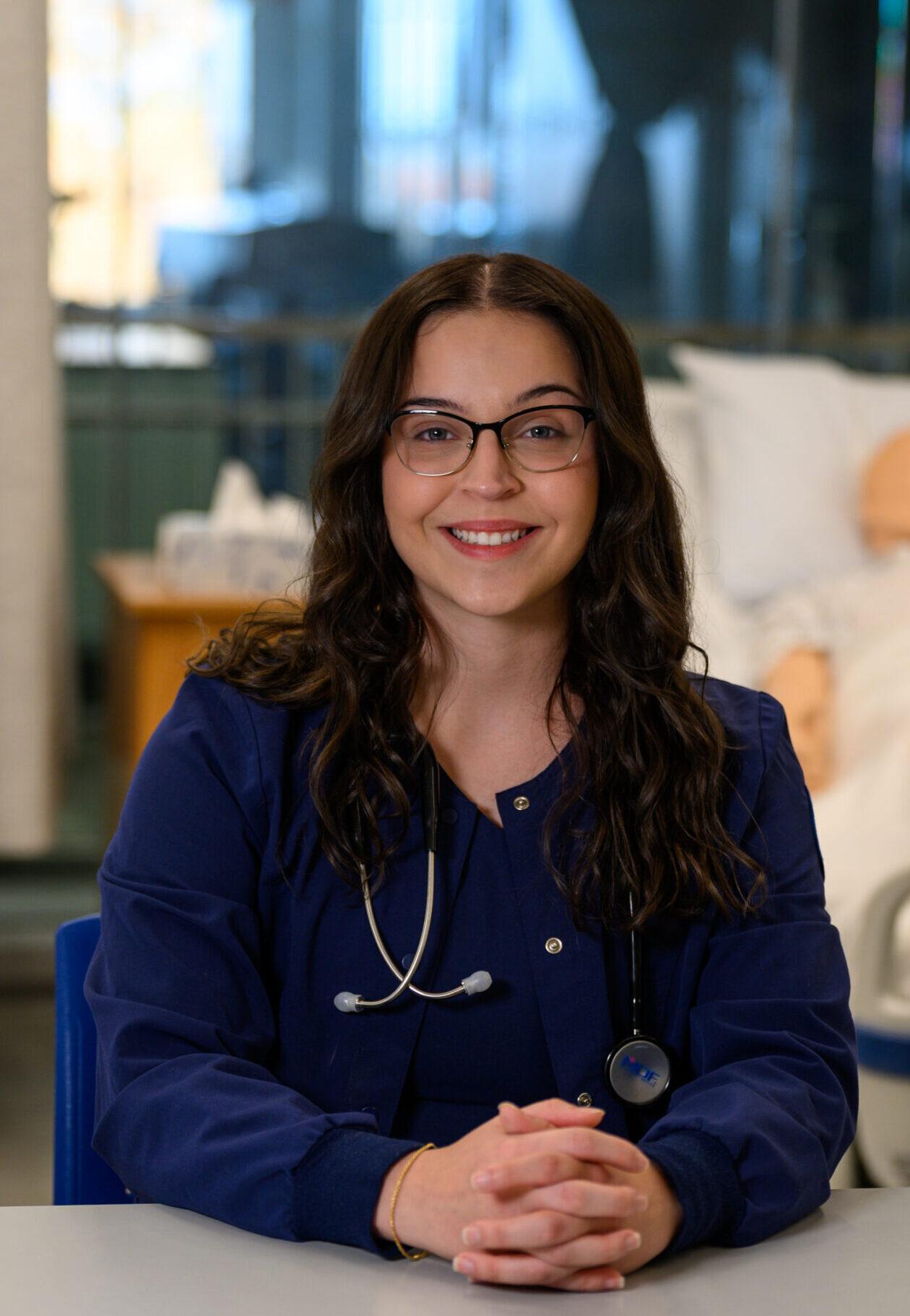 Female student wearing nursing scrubs, smiling at the camera.